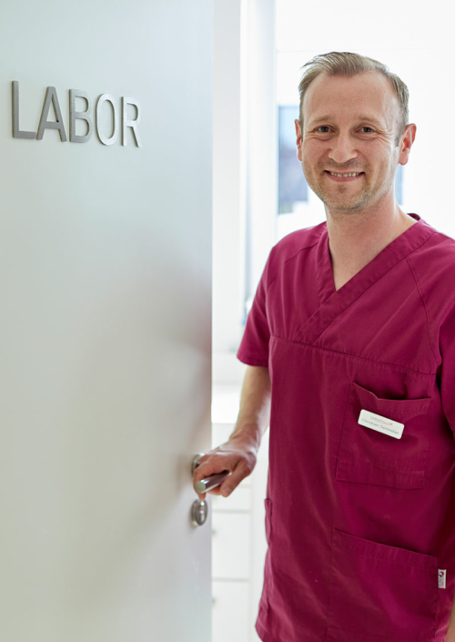 Ein Mitarbeiter von Orthoplace steht in der Tür zum Labor und hält die Klinke in der Hand