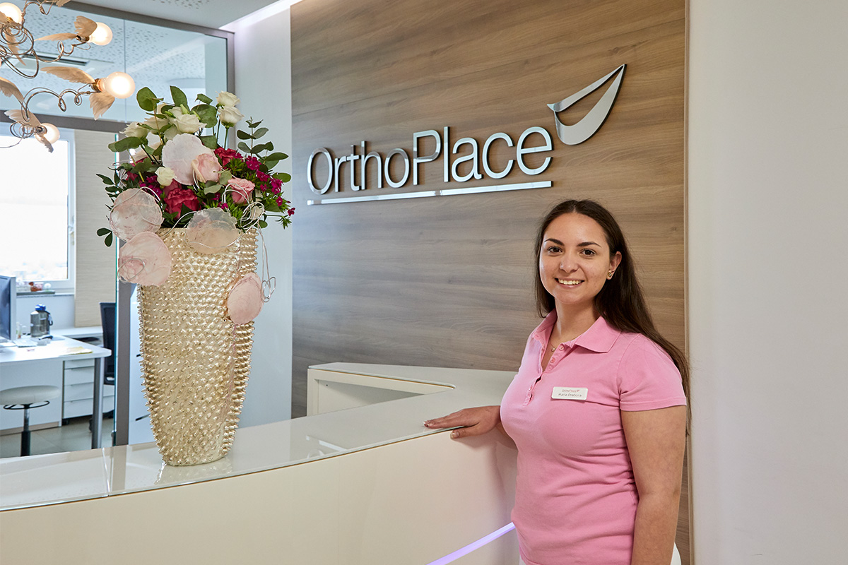 Eine Mitarbeiterin steht freundlich lächelnd an dem Anmelde-Tresen bei OrthoPlace